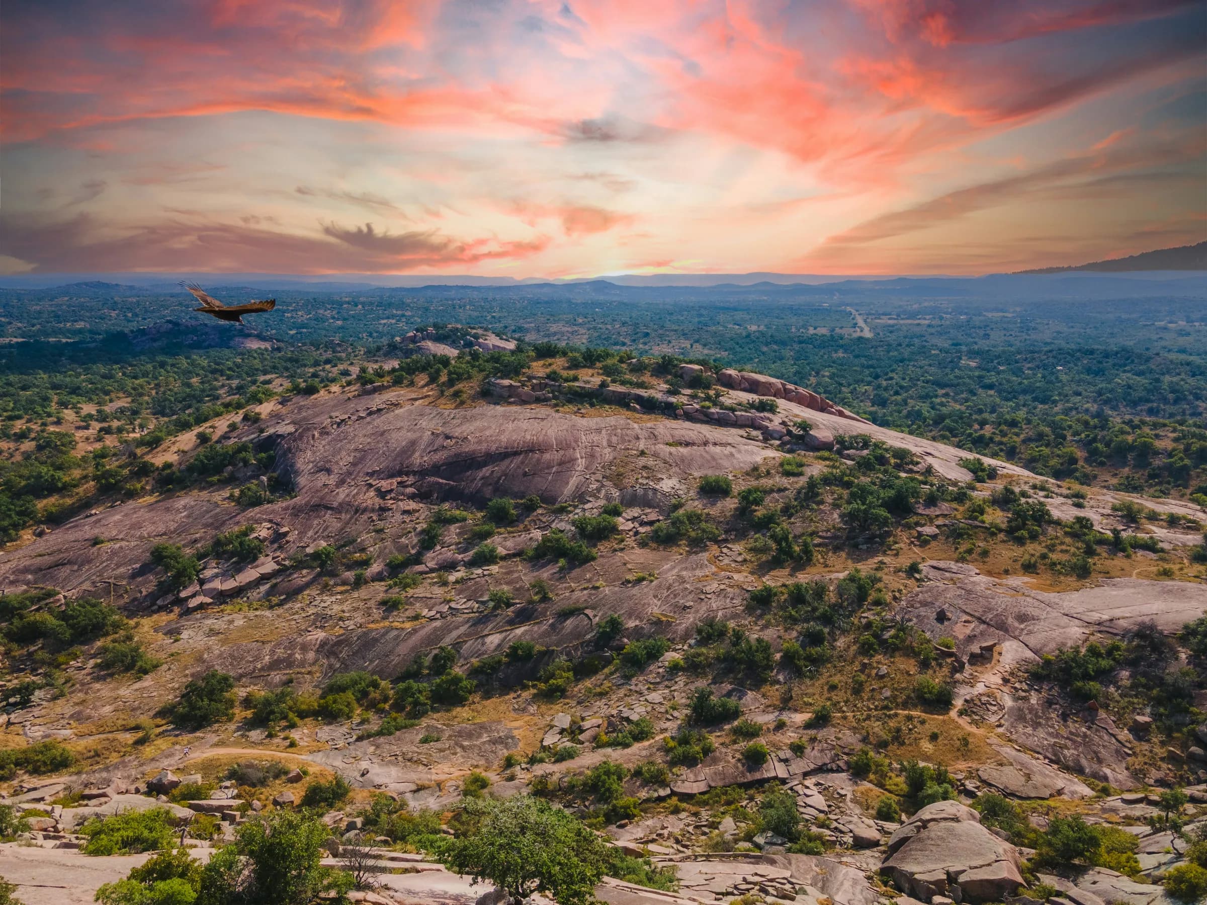 Aerial view of Enchanted Rock, Texas at sunset with a bird flying over the granite dome