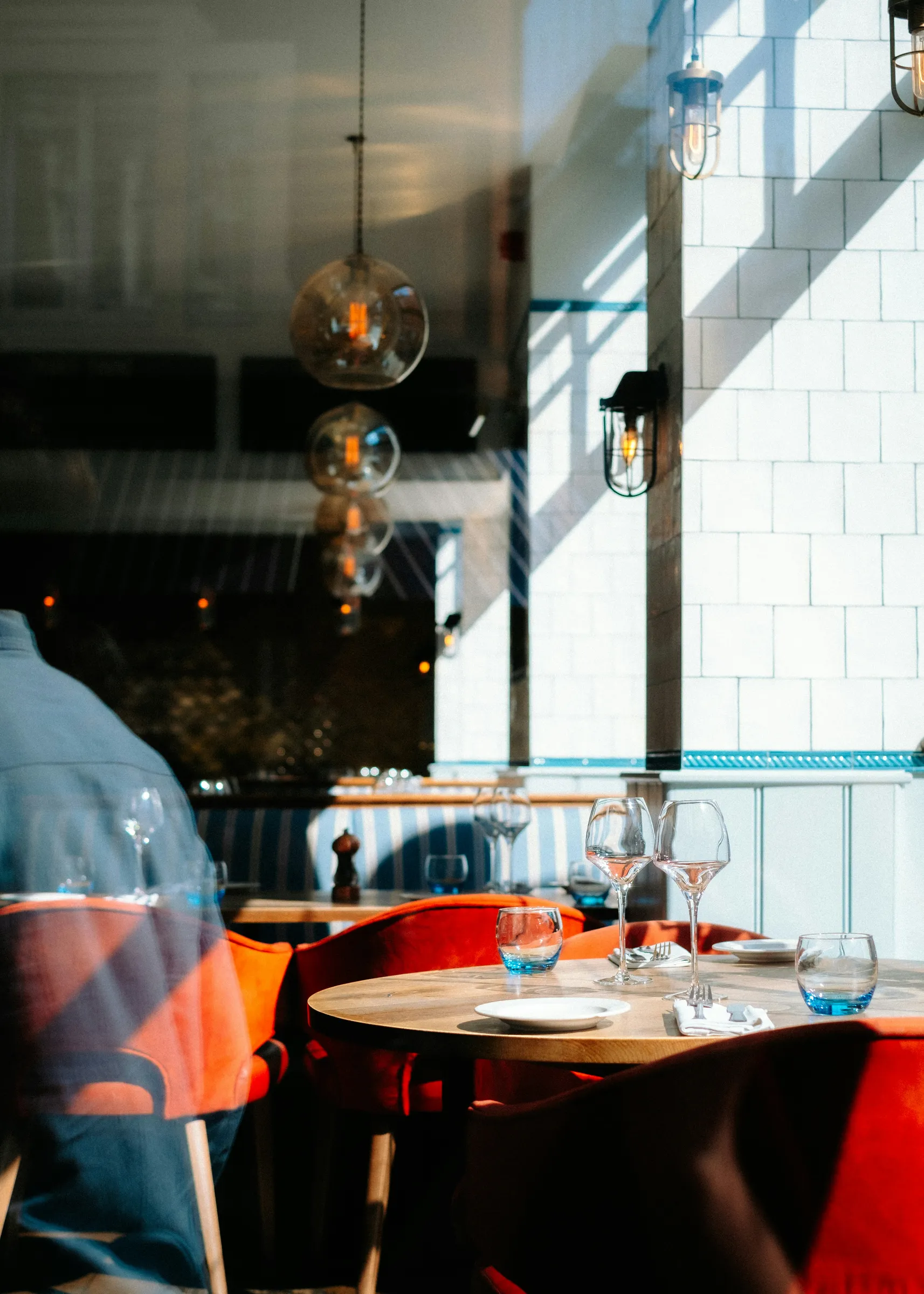 Restaurant interior with orange chairs, set table, and wine glasses in natural light
