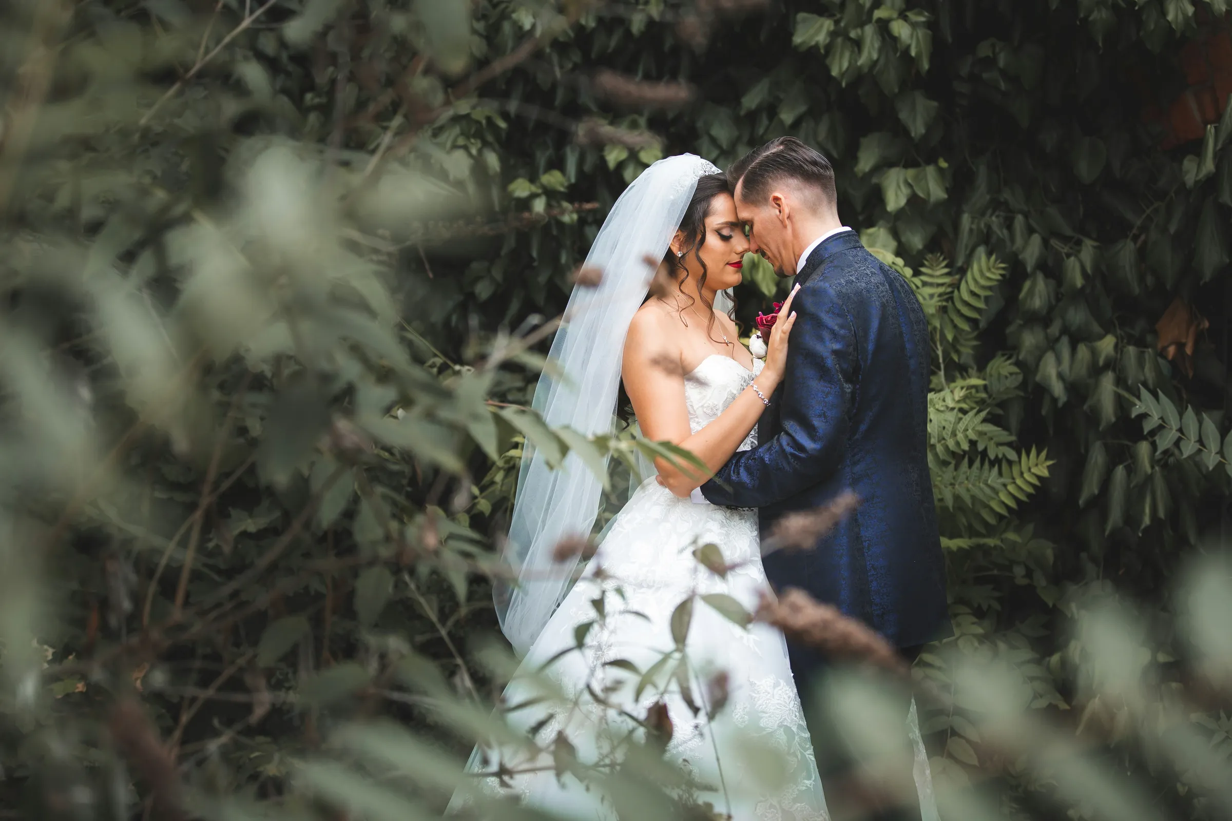 Bride and groom embracing intimately amid greenery at a wedding venue