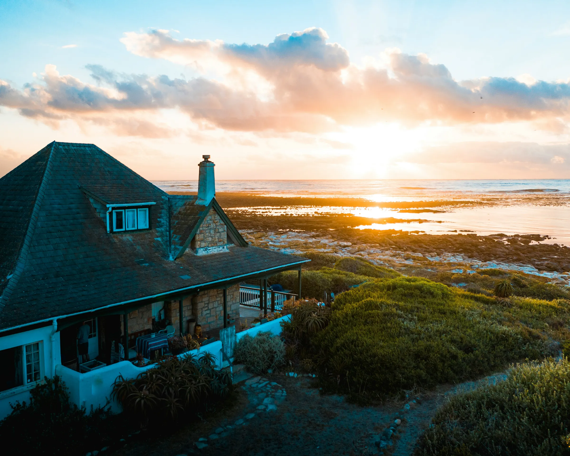 Aerial view of a coastal vacation rental cottage with ocean and sunset behind it