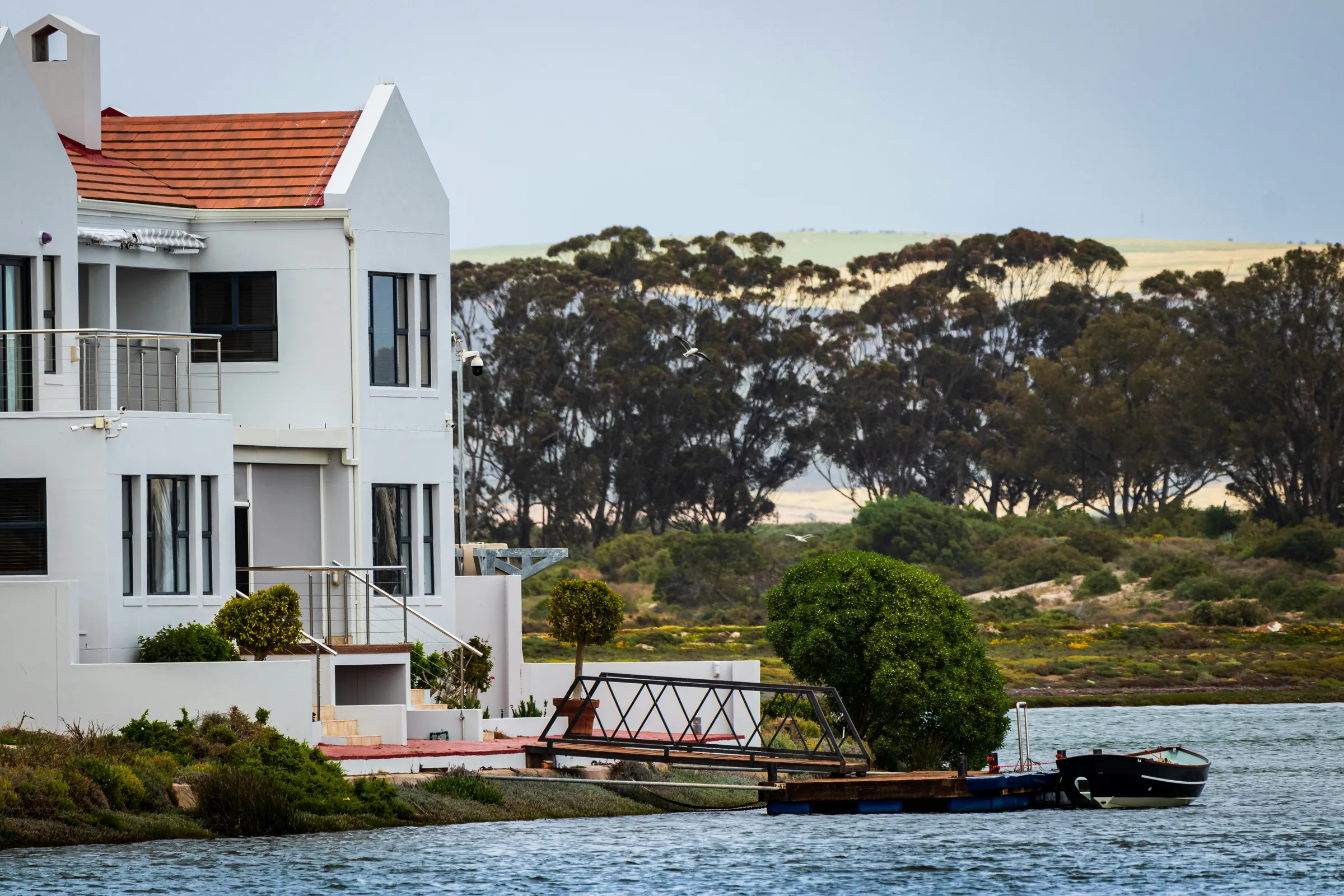 Waterfront vacation rental home with red tile roof, private dock, and boat on a calm river estuary