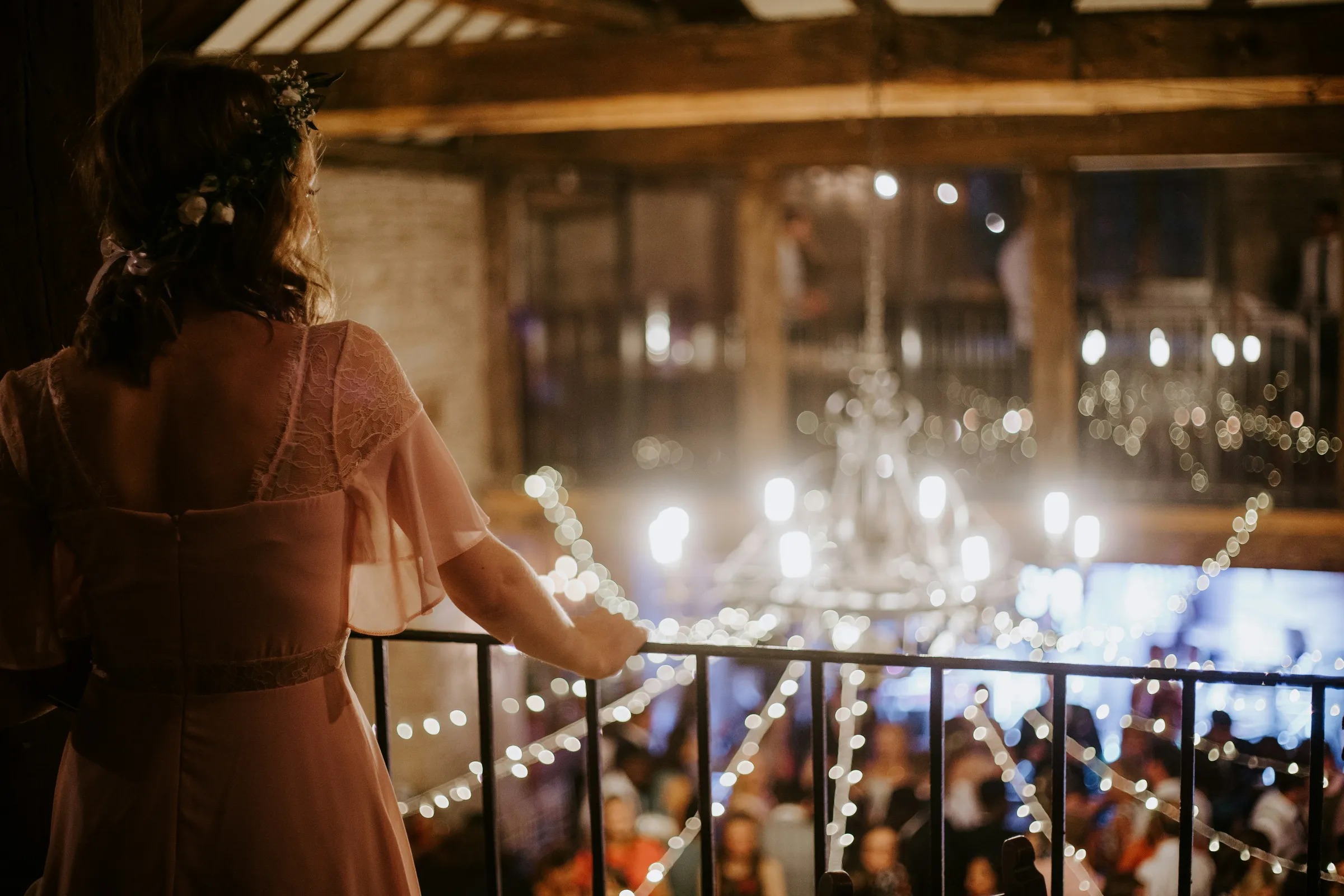 Wedding guest in a blush dress with a floral crown overlooking a reception with string lights at a wedding venue