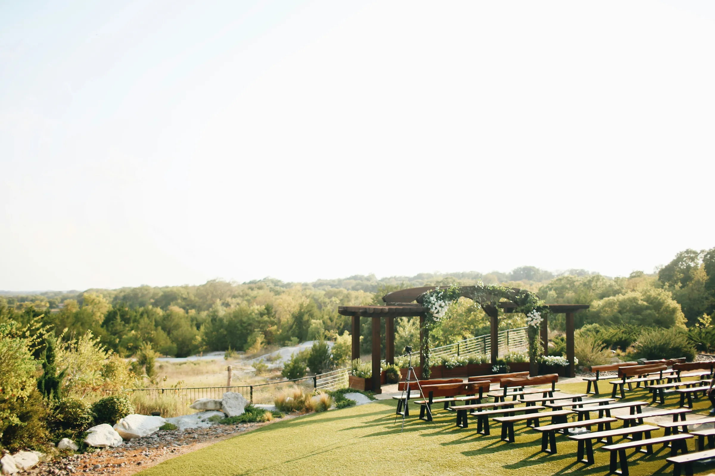 Outdoor wedding venue with a floral pergola arch and bench seating overlooking Hill Country hills