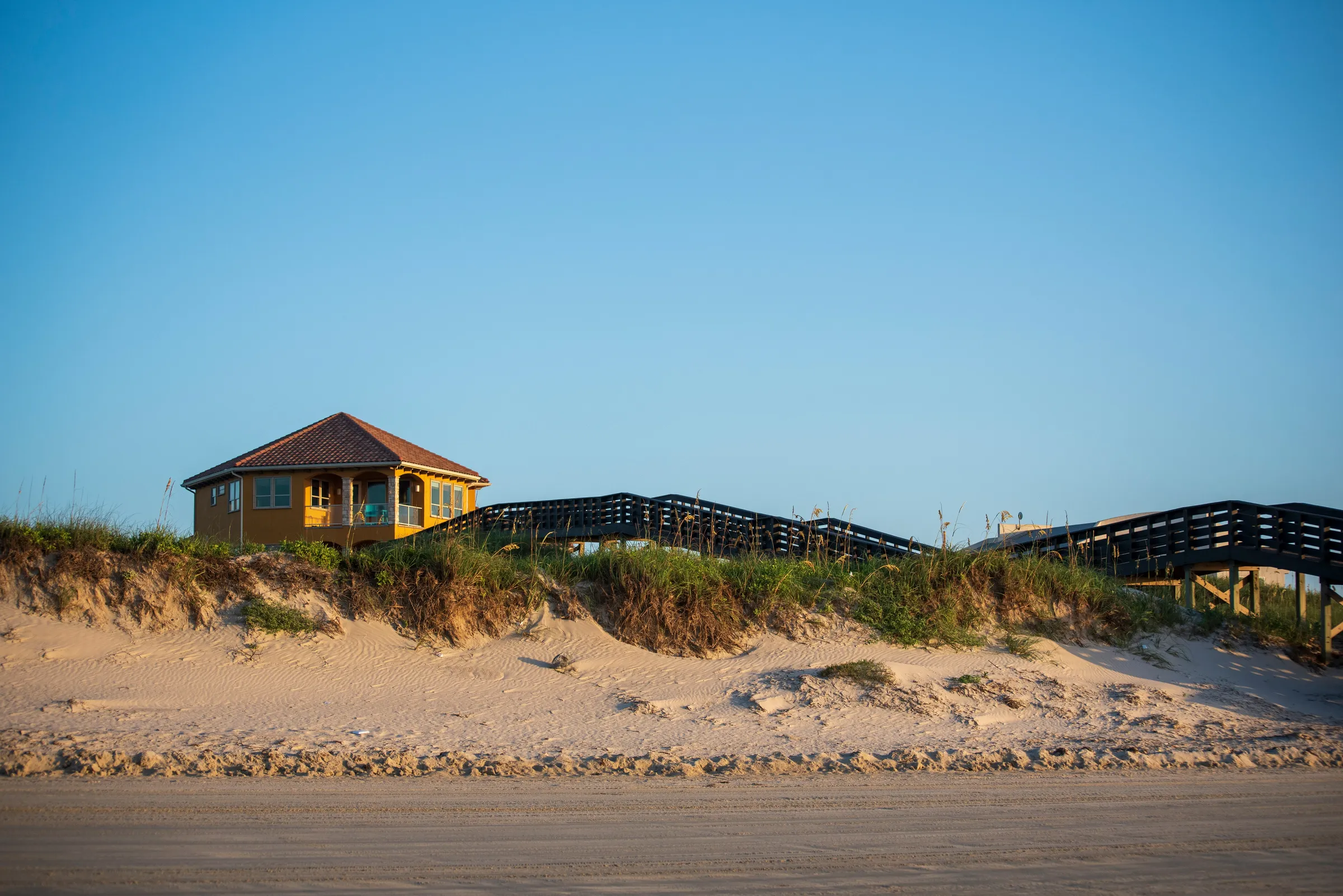 Yellow beach vacation rental home on a dune with wooden boardwalk access, viewed from the sand